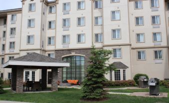 a large hotel building with a grassy courtyard in front of it , surrounded by trees at Staybridge Suites Milwaukee Airport South