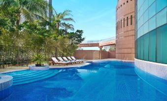a large swimming pool with a spiral - shaped tower in the background , surrounded by sun loungers and trees at Hilton Beirut Metropolitan Palace