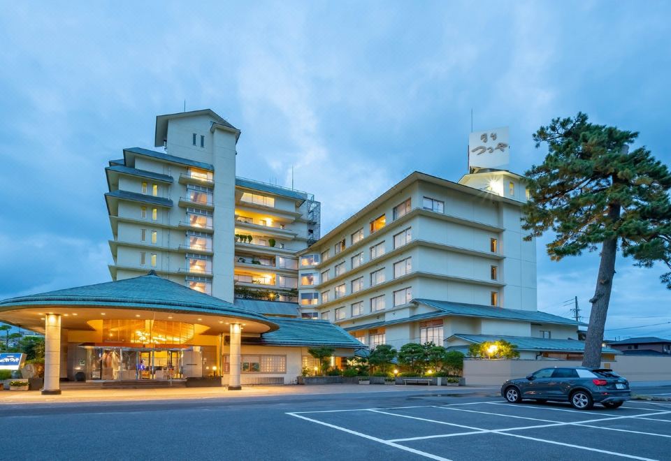 a large hotel building with multiple floors and balconies , situated in a parking lot near trees at Kaike Tsuruya