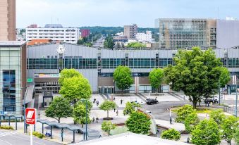 a bustling city scene with a large building , trees , and people walking around in an open area at Fukui Hotel