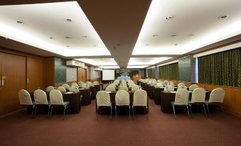 a large conference room with rows of chairs and tables , a projector screen , and natural light from the ceiling at Bay Hotel Srinakarin