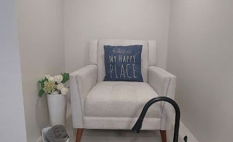 "a white armchair with a blue pillow that says "" stay happy "" is in a room with a potted plant and a bowl" at Pelican Beach Hotel