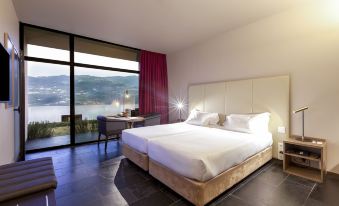 a large bed with white linens is in a room with a window overlooking the ocean at Douro Palace Hotel Resort & Spa