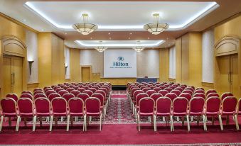a conference room with red chairs arranged in rows , a large screen on the wall , and a podium at the front at Hilton Beirut Metropolitan Palace