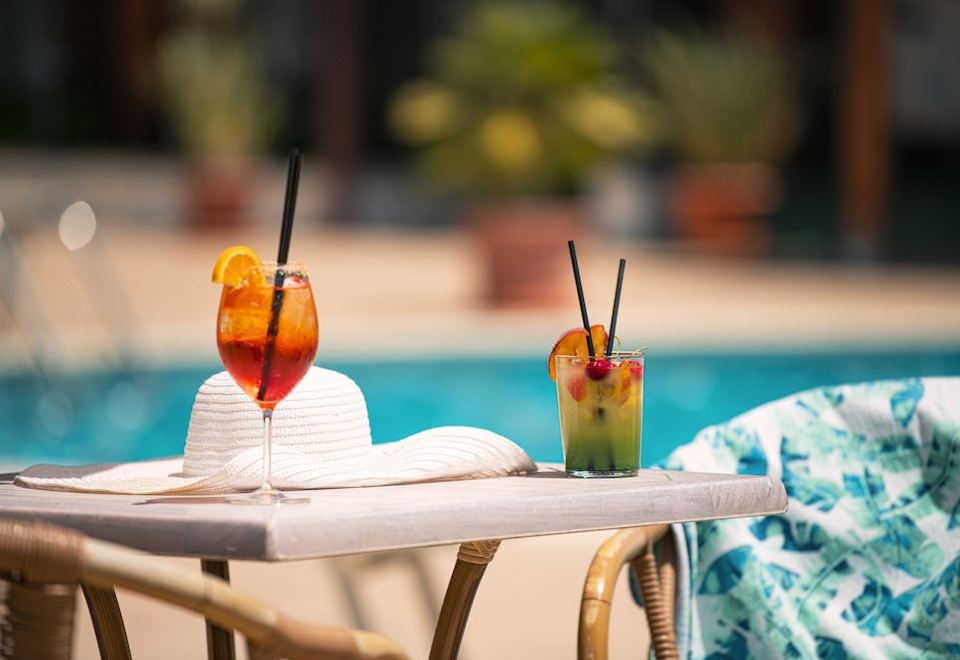 two glasses of cocktails are placed on a table near a swimming pool , with umbrellas and towels nearby at Hotel Califfo