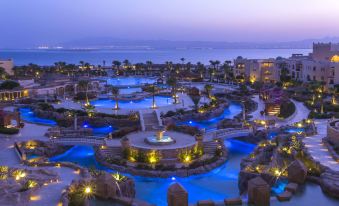 a large resort with a pool and water features is illuminated by blue lights at night at Kempinski Hotel Soma Bay