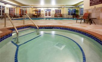 an indoor swimming pool with a hot tub , surrounded by lounge chairs and tables , in a well - lit room at Homewood Suites by Hilton Minneapolis-New Brighton