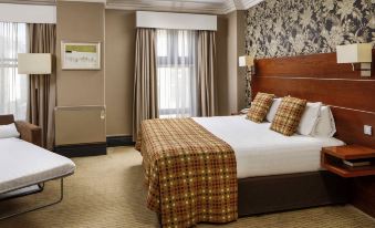 a hotel room with a king - sized bed , a television , and a bathroom in the background at Mercure Bradford Bankfield Hotel