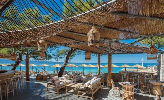 a beach bar with wooden tables and chairs , under a thatched roof , overlooking the ocean at Le Meridien Lav Split