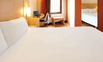 a hotel room with a bed , desk , and window , along with a view of a city skyline at Ibis Strasbourg Centre Historique