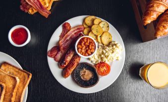 a white plate filled with a variety of food items , including bacon , potatoes , beans , and a bowl of soup at Village Hotel Cardiff