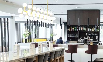 a modern bar with a long wooden counter and a person sitting at the counter at Hampton by Hilton Toulouse Airport