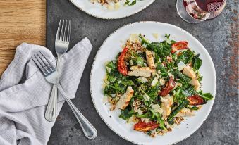 a white plate filled with a salad of chicken , tomatoes , and greens is placed on a table next to silverware and a glass of wine at Courtyard Richmond West