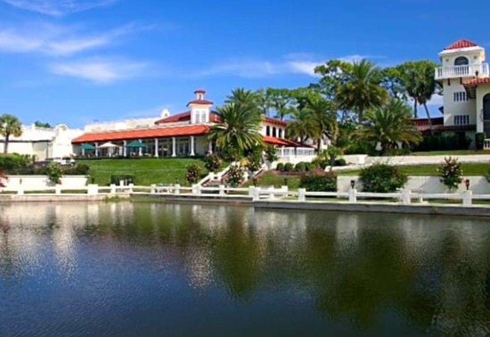 a large white building with a red roof is reflected in the water , surrounded by palm trees at Mission Inn Resort & Club