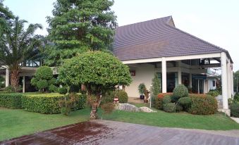 a large house surrounded by a lush green lawn , with trees and bushes in the background at Triple Resort