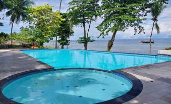 a large swimming pool with a circular design is surrounded by trees and overlooks the ocean at Asana Biak Papua Hotel