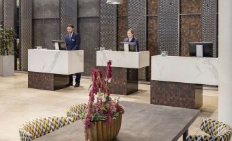 a modern hotel lobby with two reception desks , marble floors , and seating areas where customers can use their phones at NH Leipzig Zentrum