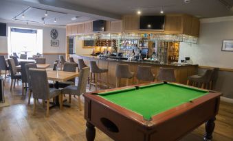 a pool table is in the center of a room with tables and chairs , as well as a bar with stools at The Inn at Brough