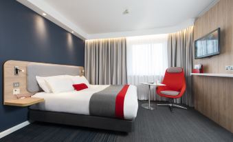 a hotel room with a large bed , red chair , and gray curtains , along with a chair in the corner at Holiday Inn Express London - Dartford