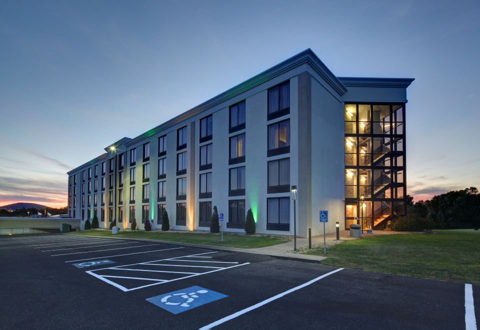 a modern , multi - story building with a green facade and large windows , illuminated by lights at night , and a handicap parking space in the at Holiday Inn Staunton Conference Center
