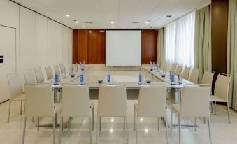 a conference room set up for a meeting , with chairs arranged in a rectangular formation and a projector on the wall at Hesperia Barcelona Sant Just