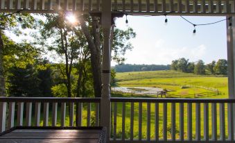 a wooden porch with a view of a field and trees , taken from inside the house at Inn at Tyler Hill