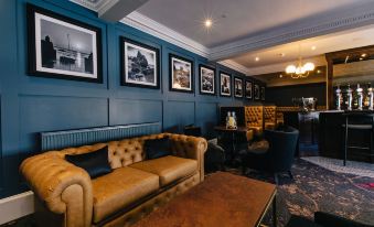 a cozy living room with a brown couch and a blue wall adorned with framed pictures at The Seafield Arms-Cullen