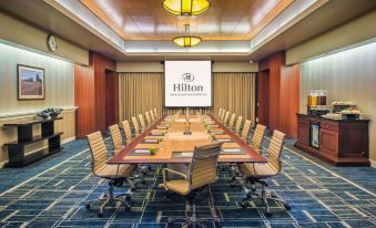 a large conference room with a long wooden table , multiple chairs , and a projector screen displaying the hilton logo at Hilton Vancouver Washington