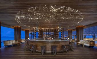 a modern bar with wooden floors , multiple stools , and a ceiling adorned with fairy lights at Anantara Kihavah Maldives Villas
