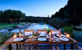 a dining table set with a variety of food and drinks , surrounded by chairs and overlooking a pool at dusk at Domaine de Peretti Della Rocca