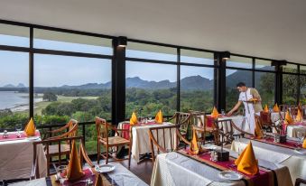 a man standing in a restaurant with large windows overlooking a scenic view of mountains at Heritance Kandalama