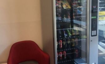 a red chair is next to a glass door with a vending machine filled with various drinks at City Edge Box Hill Apartment Hotel