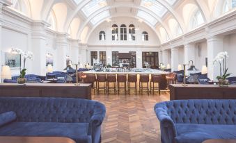 a large , white - walled room with high ceilings and arched windows , containing multiple couches and tables , as well as a bar area at Titanic Hotel Belfast