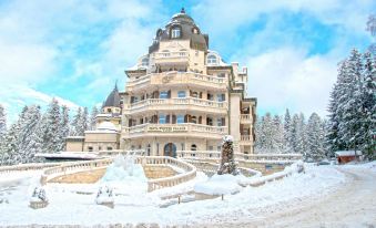 a large white building with a dome is surrounded by snow and has a ski lift in front at Festa Winter Palace Hotel