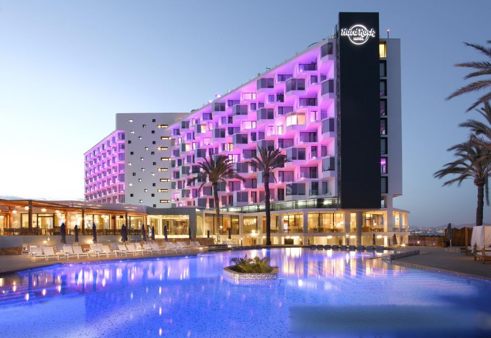 a large hotel building with a large pool in front of it , surrounded by palm trees at Hard Rock Hotel Ibiza