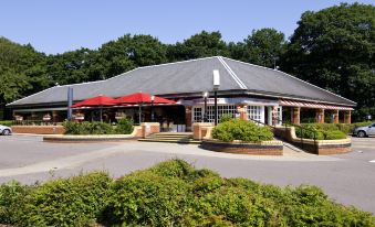 a building with a red awning and multiple umbrellas is surrounded by greenery and bushes at Premier Inn Fareham