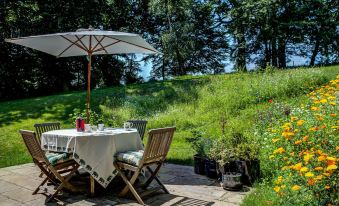 a patio with a dining table , chairs , and an umbrella is set up in a grassy area at South Park Farm Barn