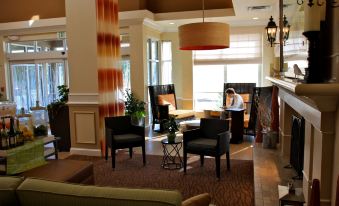 a living room with several chairs and a couch , along with a dining table in the background at Hilton Garden Inn Albany