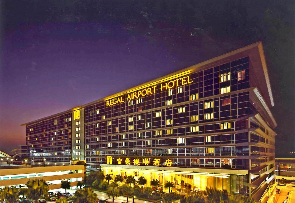 The exterior view at night showcases a large building in front with an illuminated hotel at Regal Airport Hotel