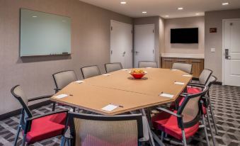 a conference room with a wooden table surrounded by chairs , and a television mounted on the wall at TownePlace Suites Merced
