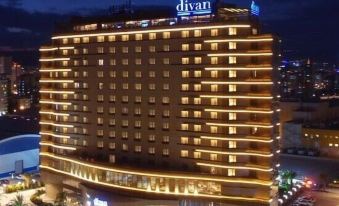 "a large hotel building with its name "" divan "" lit up at night , surrounded by other buildings and vehicles" at Divan Mersin