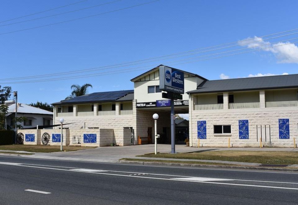 a motel with a blue sign on the side of a road , surrounded by trees at Best Western Caboolture Gateway Motel