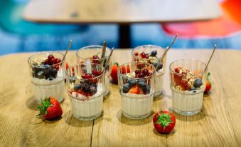 a wooden table topped with several glasses filled with yogurt and topped with berries , fruit , and nuts at Ibis de Panne