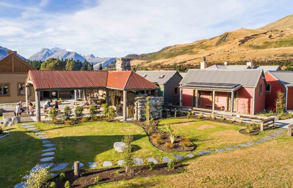 a large house with a red roof and stone walls is surrounded by greenery in front of mountains at The Headwaters Eco Lodge