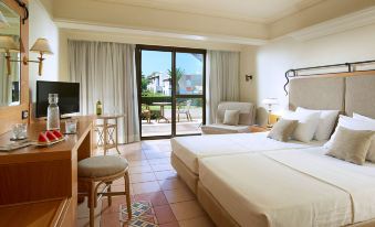 a hotel room with two beds , a television , and a sliding glass door leading to a balcony at Aldemar Knossos Royal