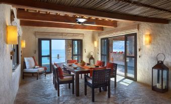 a spacious living room with large windows , wooden beams on the ceiling , and a dining table surrounded by chairs at Six Senses Zighy Bay