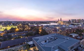 a city skyline at sunset , with buildings and trees lit up against a pink and blue sky at Oaks Sydney Goldsbrough Suites