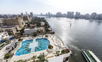 an aerial view of a large swimming pool surrounded by palm trees , with a city skyline in the background at Grand Nile Tower