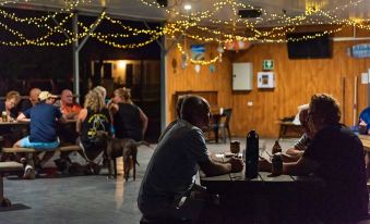 a group of people sitting at a bar with string lights , enjoying drinks and conversation at Discovery Parks - Tannum Sands