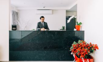 a man in a suit standing behind a reception desk , surrounded by potted plants and flowers at Voyager Motel